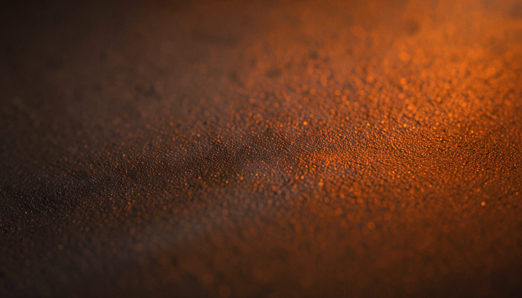 Close-up of dark matte material with subtle grain, warm amber light grazing the surface