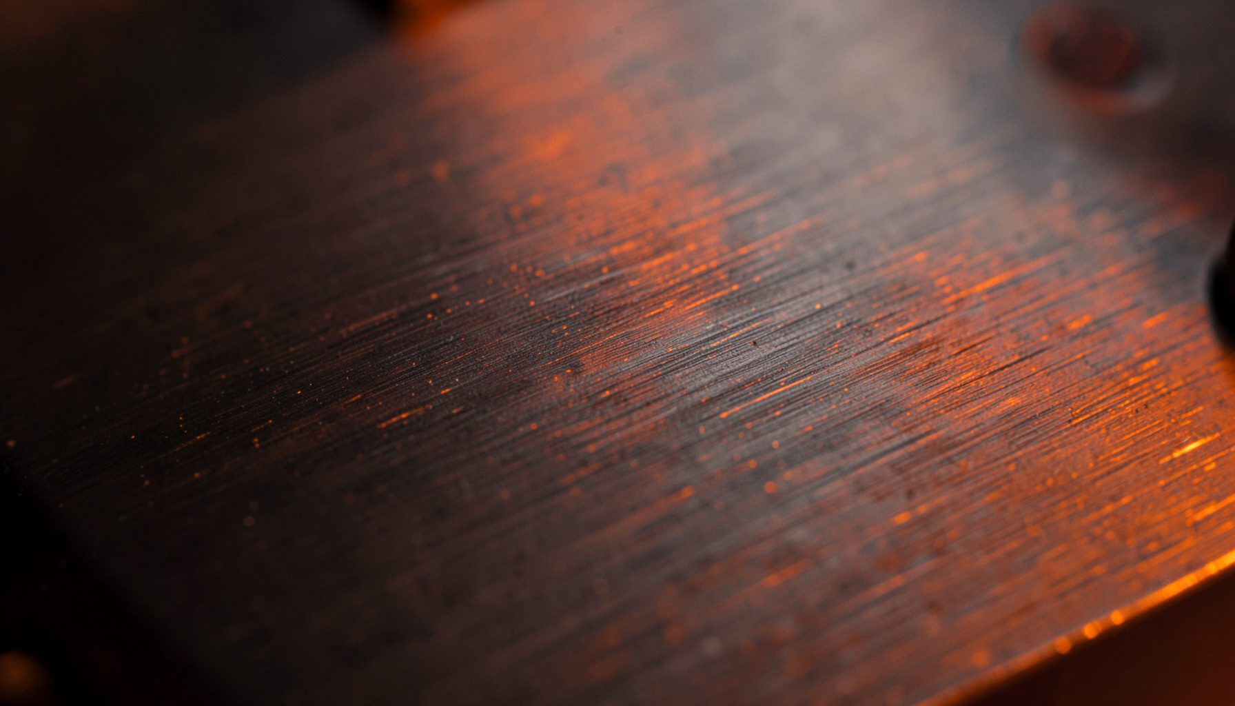 Close-up of dark brushed metal with faint orange highlights, industrial and clean