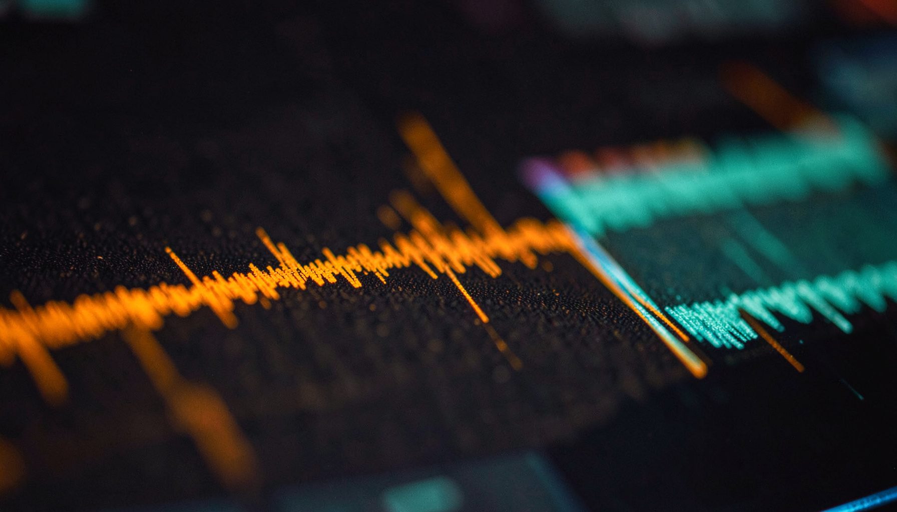 Close-up of a digital audio workstation waveform on a dark screen with warm amber and teal track colors