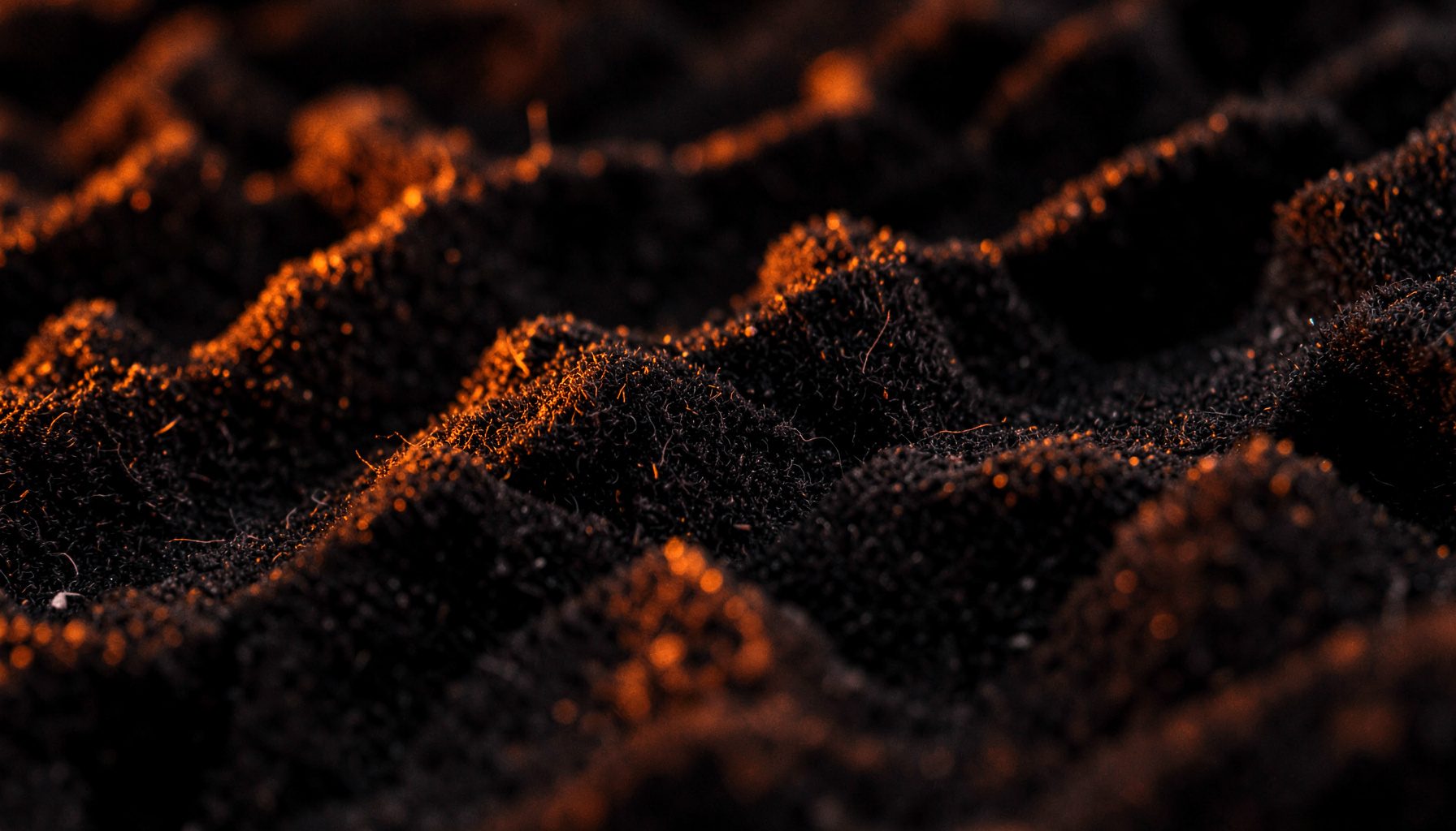 Extreme close-up of dark charcoal acoustic foam texture with subtle orange light bleeding across the peaks and valleys