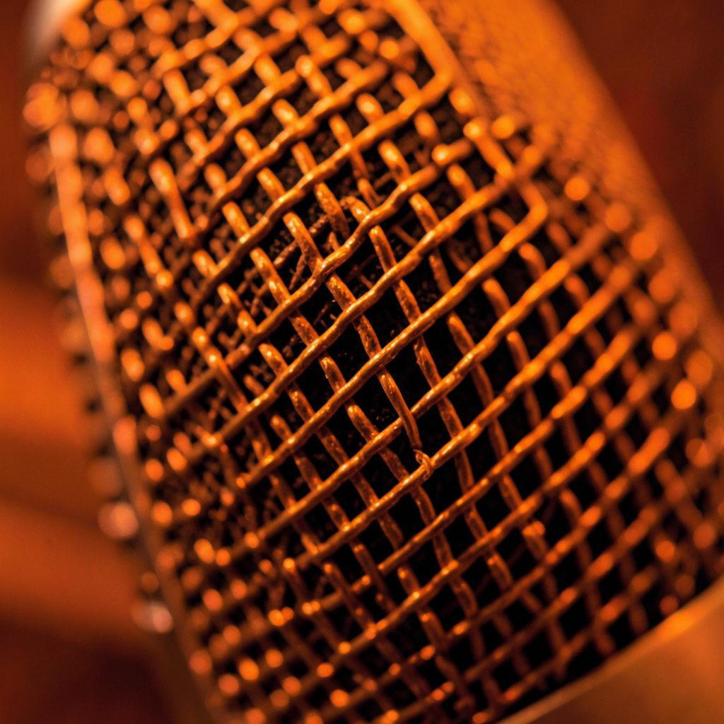 Warm amber and deep brown tones of a vintage microphone grille in extreme close-up, soft bokeh background