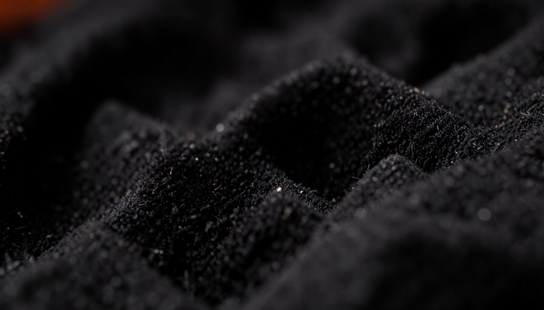 Extreme close-up photograph of dark charcoal acoustic foam texture, with deep shadowed valleys and soft matte peaks, moody studio atmosphere
